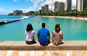 Three people are sitting on a wall overlooking the ocean.