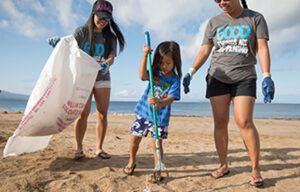 Two women and a little girl are cleaning the beach.