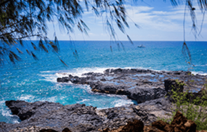 A view of the ocean from a rocky shoreline with a boat in the distance.