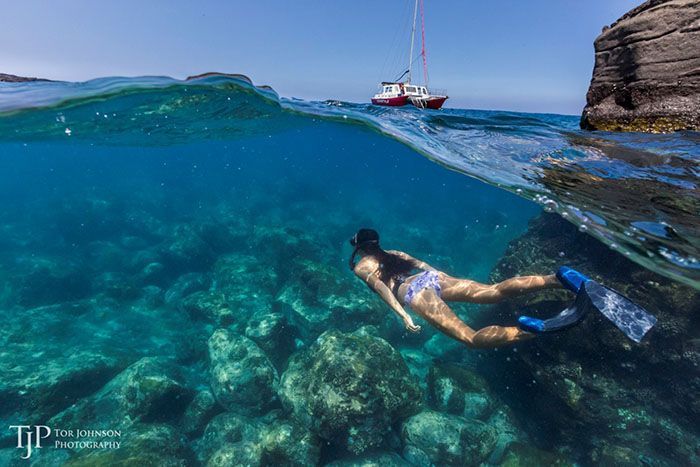 A woman is swimming in the ocean with a boat in the background.
