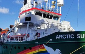 A large ship with a rainbow painted on the side is docked in a harbor.