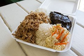 A styrofoam container filled with food is sitting on a wooden table.