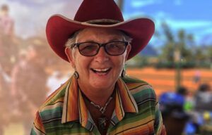 A woman wearing a red cowboy hat and glasses is smiling.