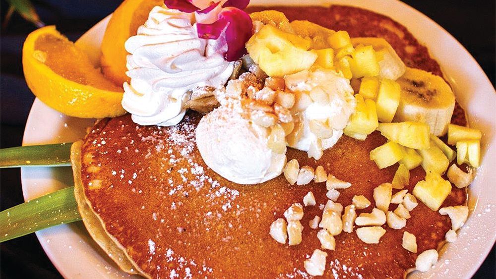 A close up of a pancake with bananas , whipped cream and pineapple on a plate.