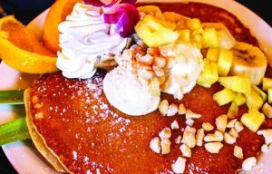 A close up of a pancakes with bananas and whipped cream on a plate.