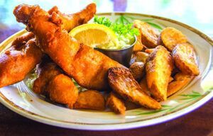 A plate of fish and chips with a lemon wedge on a table.