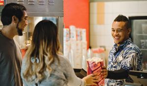 A man is selling popcorn to a woman in a movie theater.