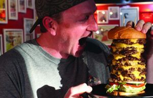 A man is eating a very tall hamburger on a plate