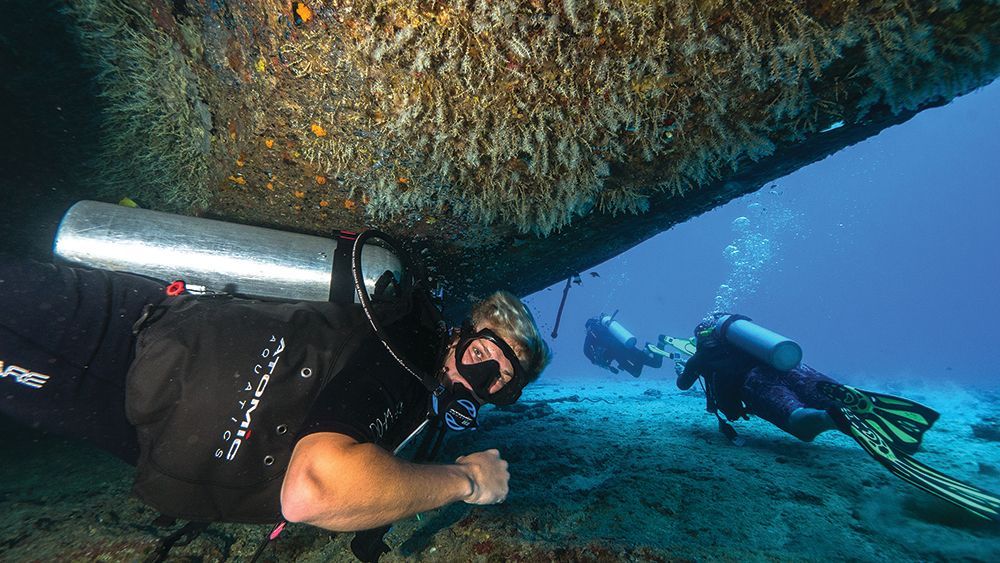 A group of scuba divers are looking under a boat in the ocean.