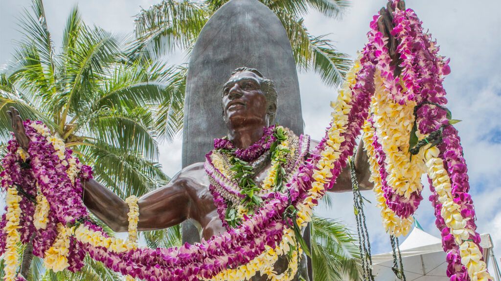 A statue of a man is surrounded by lei and flowers.