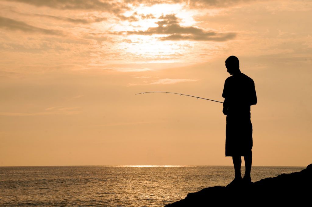 A man is standing on a cliff overlooking the ocean at sunset