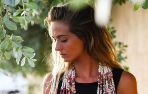 A woman wearing a scarf around her neck is standing under a tree.