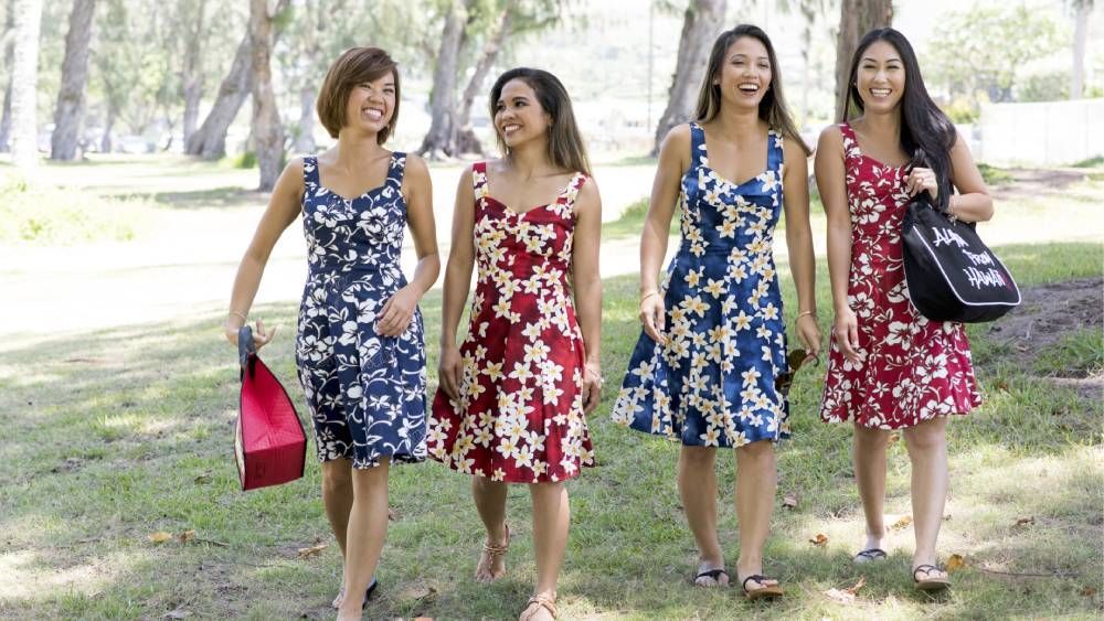 Four women in hawaiian dresses are walking in a park.