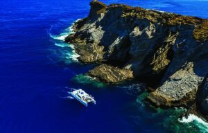 An aerial view of a boat in the ocean near a cliff.