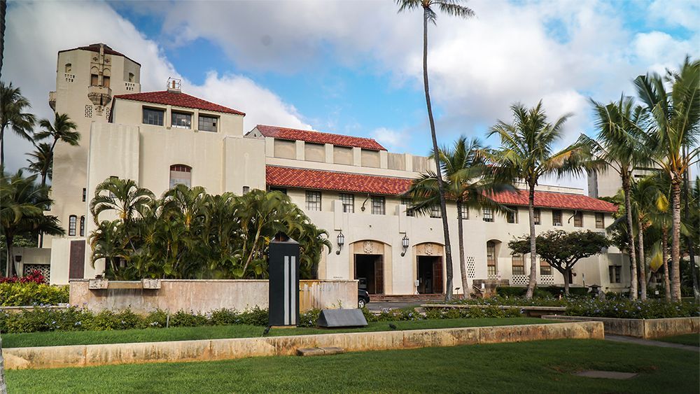 A large white building with a red tile roof is surrounded by palm trees