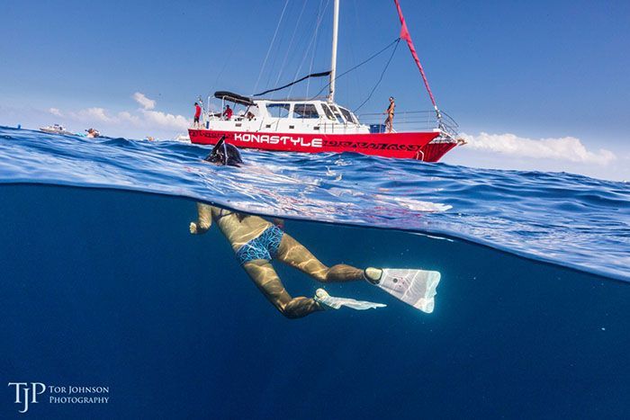 A woman is swimming in the ocean next to a sailboat.