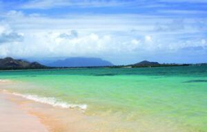 A blurred image of a beach with mountains in the background and a turquoise ocean.