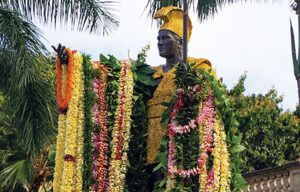 A statue of a man is surrounded by lei and flowers.