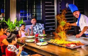 A family is sitting at a table in front of a chef cooking food.