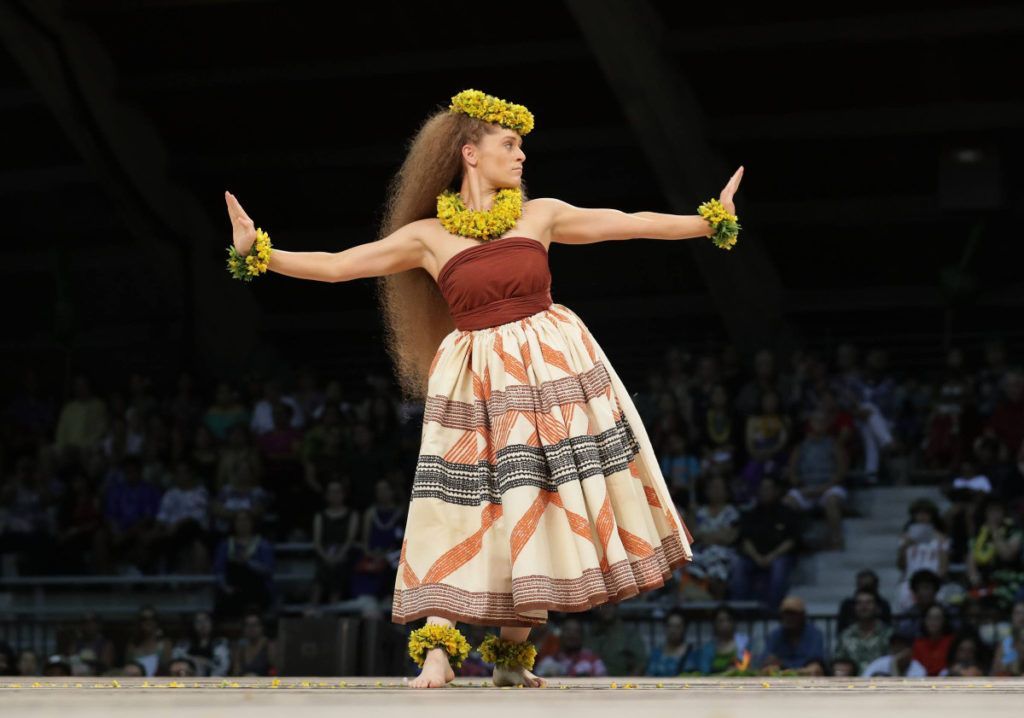 A woman in a hawaiian dress is dancing in front of a crowd.