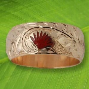 A gold ring with a flower on it is sitting on a green leaf.