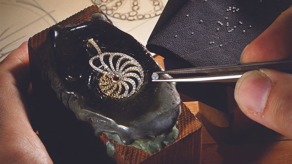 A person is working on a piece of jewelry with tweezers.