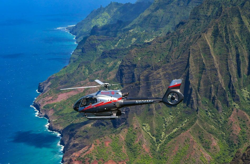 A helicopter is flying over a cliff overlooking the ocean.
