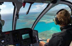 A woman wearing headphones is flying a helicopter over the ocean.