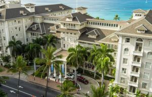 An aerial view of a large white building with palm trees in front of it.