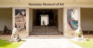 The entrance to the honolulu museum of art with statues in front of it.
