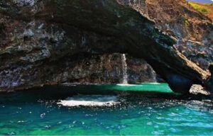 A waterfall is coming out of a cave in the middle of a body of water.
