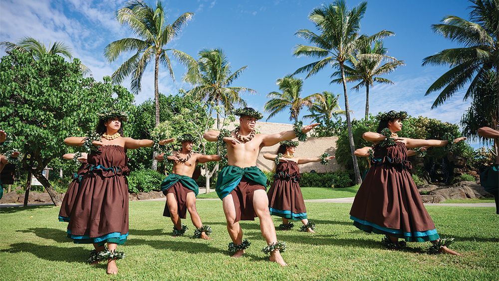 A group of people are dancing in a field with palm trees in the background.