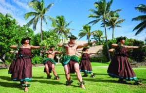 A group of people are dancing in a field with palm trees in the background.