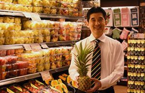 A man in a tie is holding a pineapple in a grocery store.