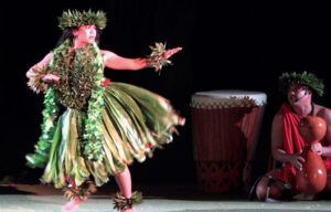 A woman in a green skirt is dancing on a stage next to a man playing a drum.