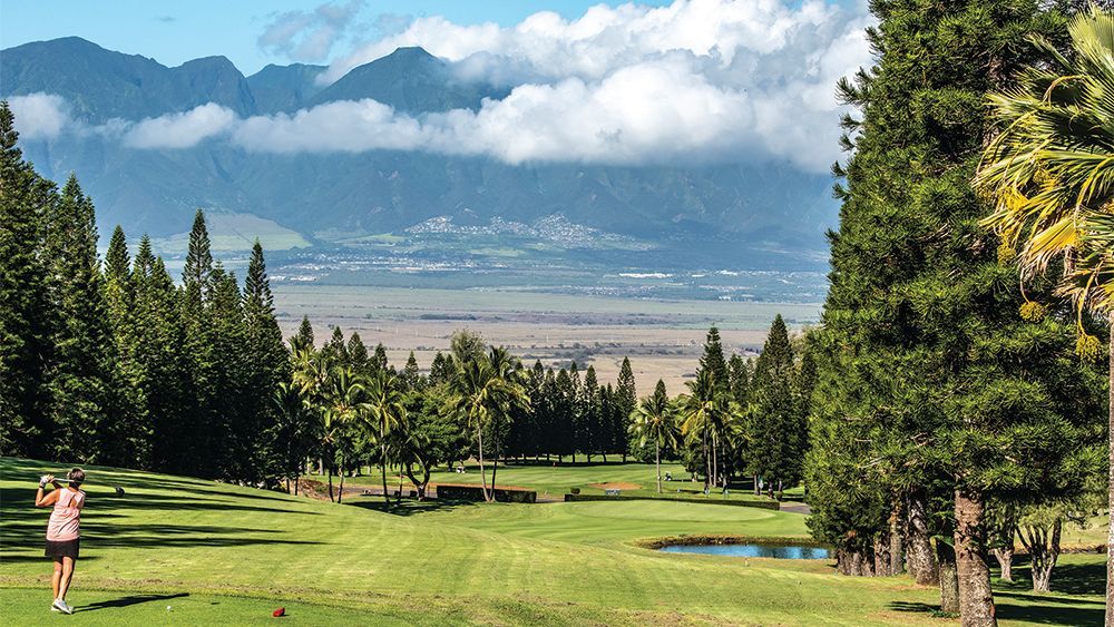 A woman is playing golf on a golf course with mountains in the background.
