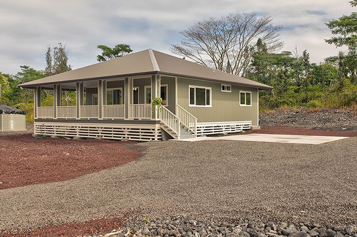 A house with a porch is sitting on top of a gravel lot.