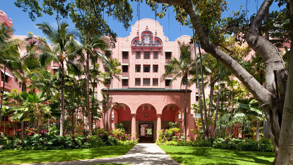 A large pink building is surrounded by trees and grass.