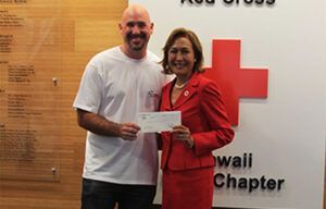 A man and a woman are holding a check in front of a red cross.