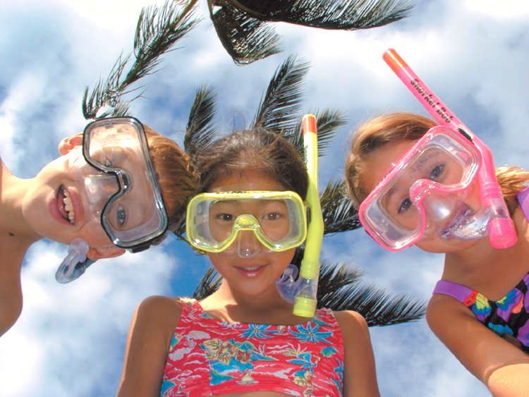 Three girls wearing goggles and snorkels are looking up at the camera