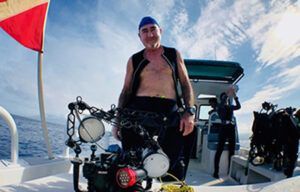 A man without a shirt is standing on a boat in the ocean.