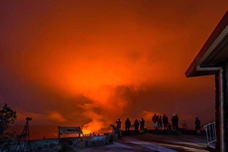 A group of people are standing on top of a hill watching a volcano eruption.