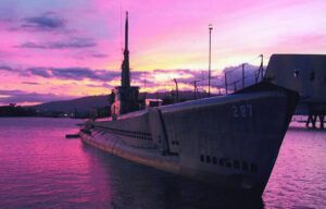 A submarine is docked in the water at sunset.