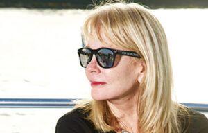 A woman wearing sunglasses and a black shirt is standing in front of a body of water.