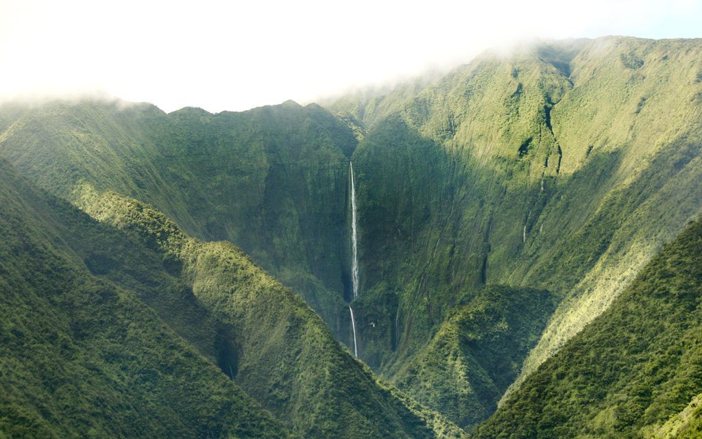 There is a waterfall in the middle of a valley surrounded by mountains.