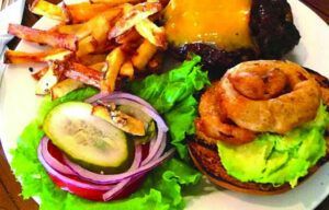 A white plate topped with a hamburger , onion rings , french fries and pickles.