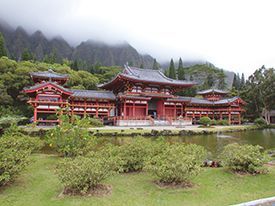 A large red building with a pond in front of it and mountains in the background.