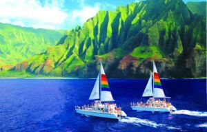 Two sailboats are floating in the ocean with mountains in the background.