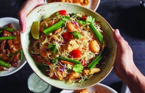 A person is holding a bowl of noodles and vegetables.