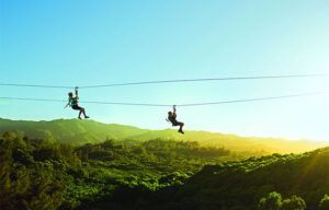 Two people are flying through the air on a zip line.